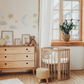 a baby's room with a crib, dresser, and window